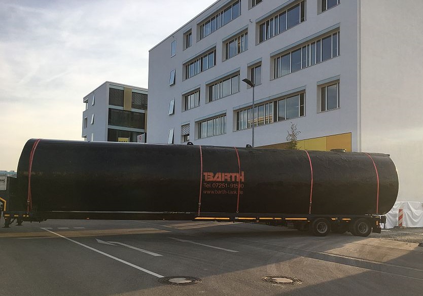 ein schwarzer 100.000 Liter Erdtank für Regenwasser von der Firma Tank und Apparate Barth GmbH wird auf einem LKW auf die Baustelle angeliefert