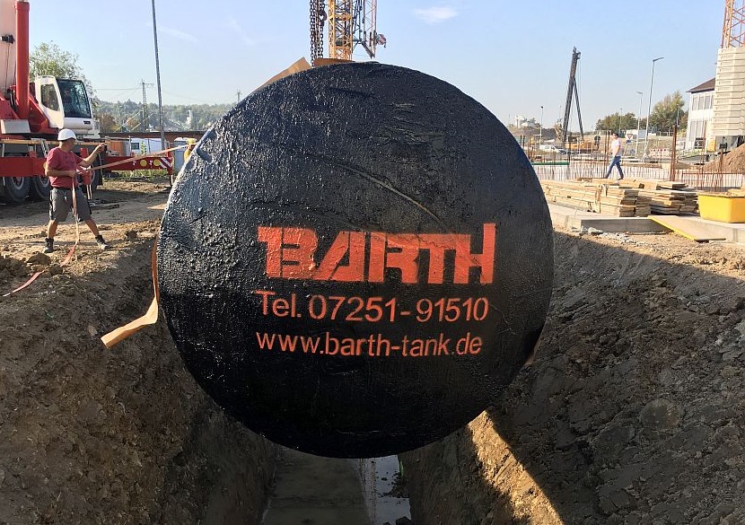 ein 100.000 l Regenwasserbehälter der Firma Tank ud Apparate Barth GmbH wird von einem Bauarbeiter in die richtige Position zum Ablassen in die Baugrube gebracht