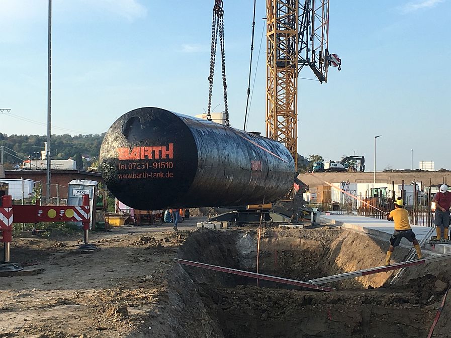 an Kran hängender schwarzer Wassertank der Firma Tank und Apparate Barth GmbH wird in Baugrube abgelassen