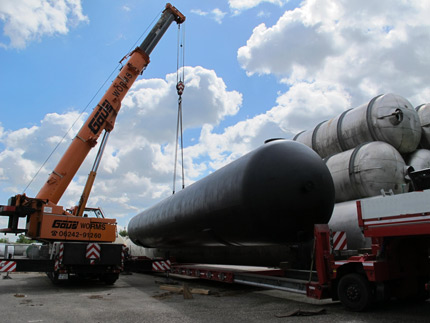 Kran hebt auf Freigelände 170.000 Liter Retentionstank mit Bitumen-Anstrich für Erdeinbau auf LKW; im Hintergrund weitere Behälter der Firma Tank und Apparate Barth GmbH